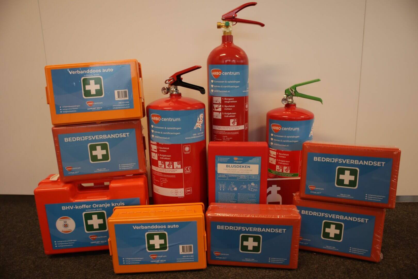 Een verzameling noodvoorraden, perfect voor degenen die veiligheidsartikelen willen aanschaffen, bevat verschillende brandblussers en verschillende oranje en blauwe EHBO-kits. De kits worden tegen een effen achtergrond weergegeven en zijn gelabeld in het Nederlands, met vermelding van items als EHBO- en zakelijke sets.