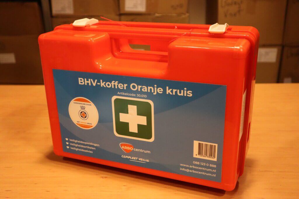 Opvallend is een feloranje EHBO-doos met een wit kruis op een groene achtergrond, met het opschrift BHV-koffer Oranje kruis, compleet met contactgegevens en streepjescode. Gesloten en rustend op hout, benadrukt het 3 voordelen van de laten keuren van de EHBO-koffer voor gemoedsrust te midden van omringende dozen.