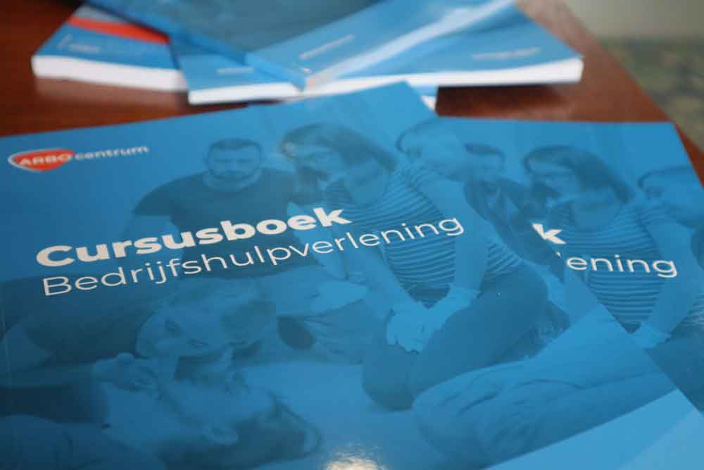 Close-up van blauwe cursusboeken over Bedrijfshulpverlening met op de cover mensen die reanimatie uitvoeren. Deze dingen leer je bij onze BHV cursus, die essentiële vaardigheden biedt. De boeken zijn netjes opgestapeld op een houten oppervlak.