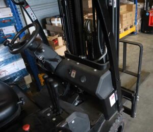 Het interieur van een magazijnheftruck onthult het stuurwiel, de hendels en het bedieningspaneel. Planken vol met dozen en pakketten doemen op in de industriële setting. Het is duidelijk waarom het behalen van een heftruckcertificaat essentieel is om zon omgeving onder de knie te krijgen.