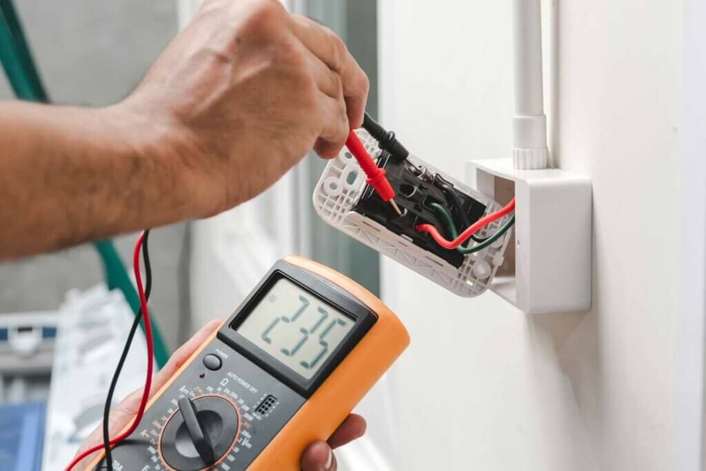 Een persoon gebruikt een digitale multimeter om de spanning bij een stopcontact te meten, om de veiligheid te garanderen zoals bepleit door het NEN 3140-certificaat. Het display geeft 235 volt aan. De oranje multimeter benadrukt de toewijding van de persoon aan de juiste techniek door de probes stevig in de open behuizing te houden.