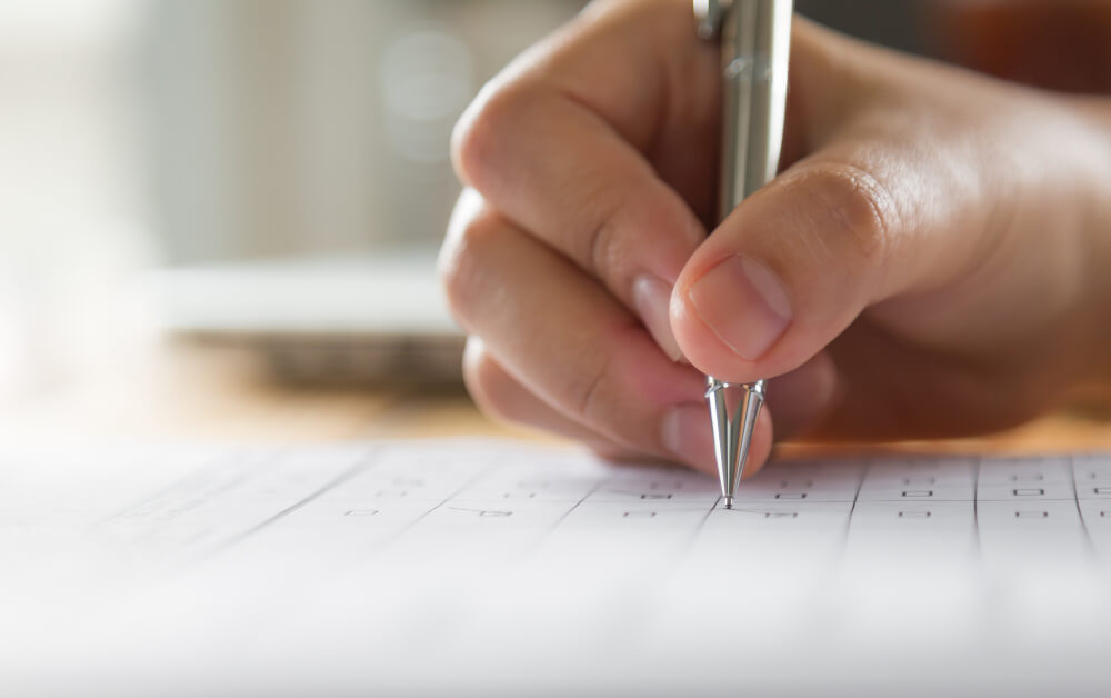 Close-up van een hand die een pen vasthoudt en schrijft op een vel papier met een rasterpatroon. Het is vergelijkbaar met voorbereiden met de voordelen van een VCA proefexamen, waarbij oefening en precisie de weg vrijmaken voor succes.