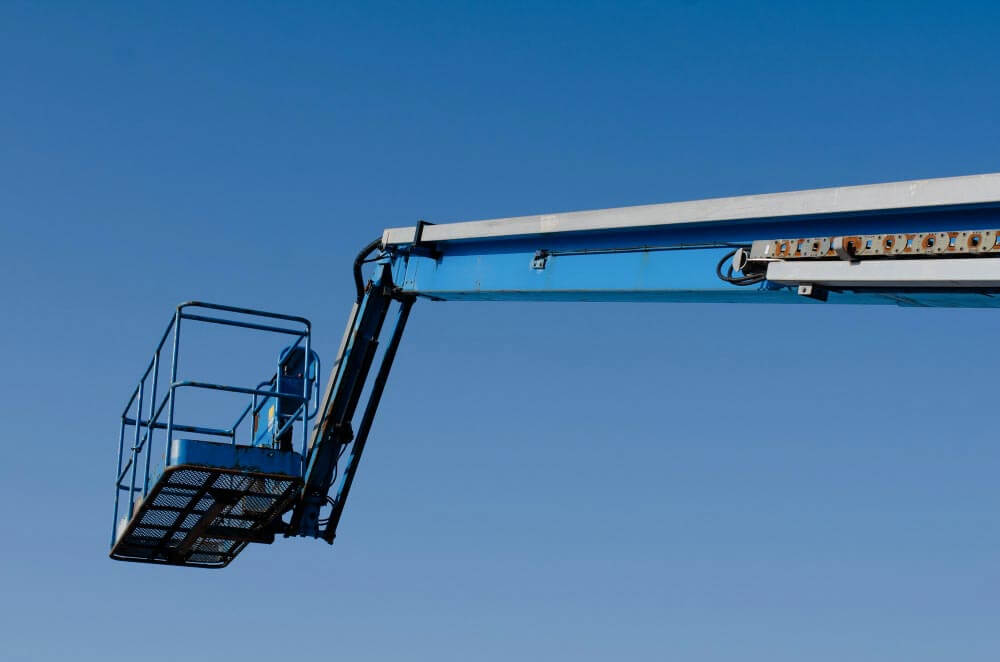 Een blauwe telescoophoogwerker strekt zich uit in de heldere lucht, de lege mand is uitgerust met een gaasvloer en veiligheidsleuning. De constructie contrasteert scherp met de achtergrond en herinnert de operators aan 4 manieren om veilig met de hoogwerker te werken voor meer veiligheid op hoogte.