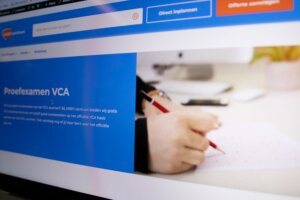 Een computerscherm met een webpagina voor Proefexamen VCA benadrukt 3 redenen om VCA proefexamens te maken. De pagina bevat een blauw gedeelte met tekst en een afbeelding van iemand die een rood potlood vasthoudt en op papier schrijft. Het bovenste menu bevat opties zoals Direct Inplannen.